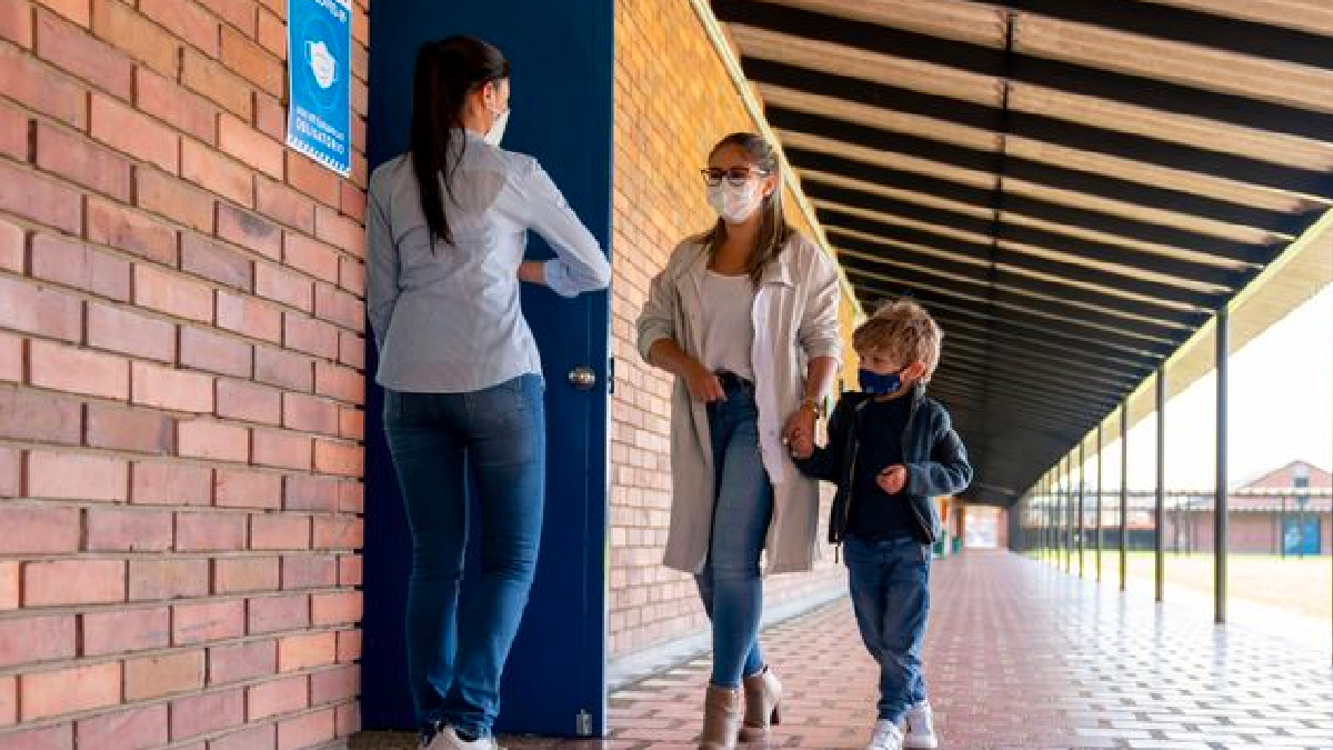 mother and son being greeted by teacher at door to classeoom