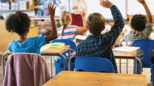 students at desks in classroom with raised hands