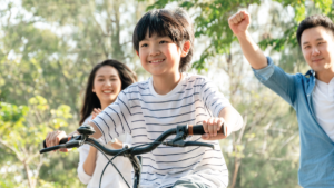 young boy riding bike as parents cheer him on in background