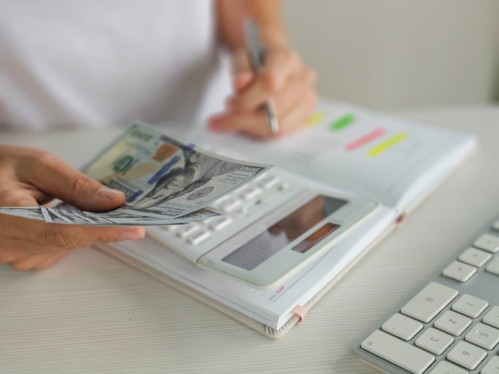 closeup of woman's hands using calculator and stacks of dollar bills