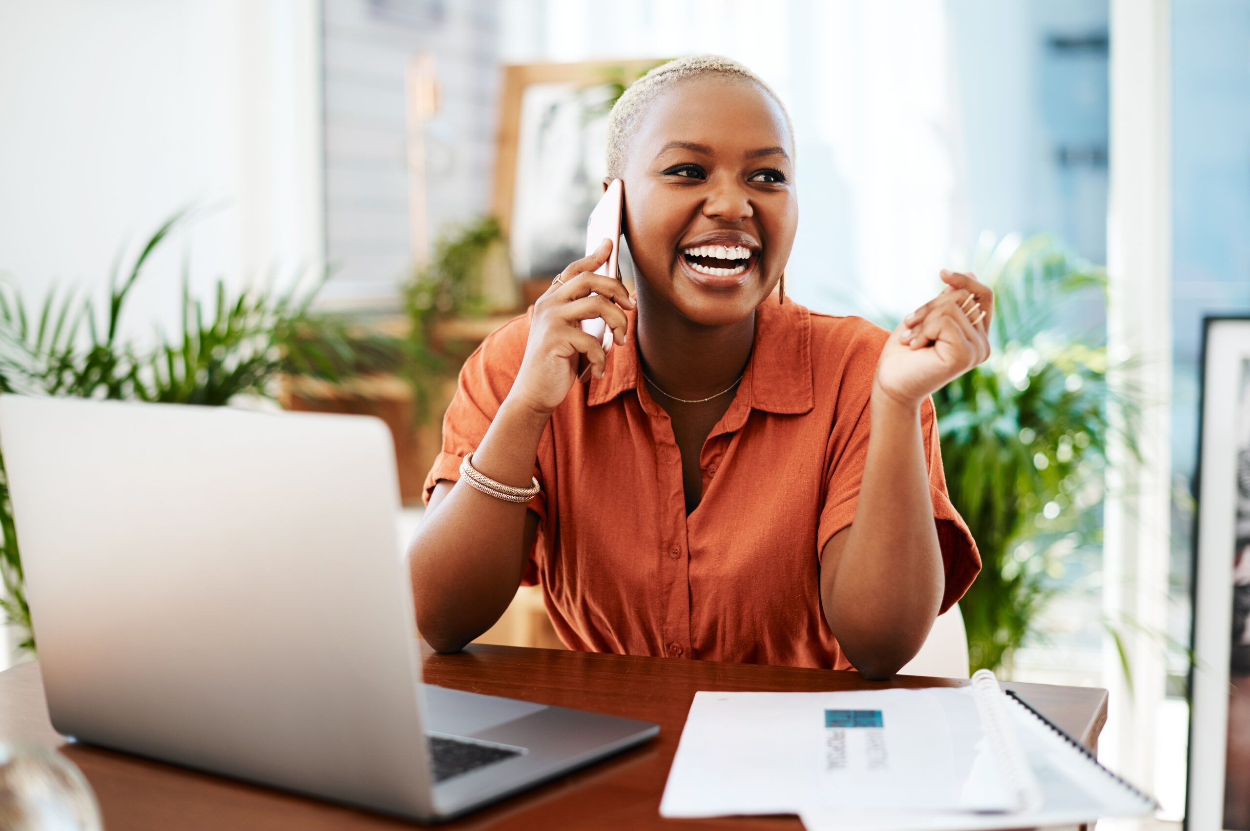 A Black woman in an office talking on the phone. She is on her smartphone and having a funny conversation, discussion,