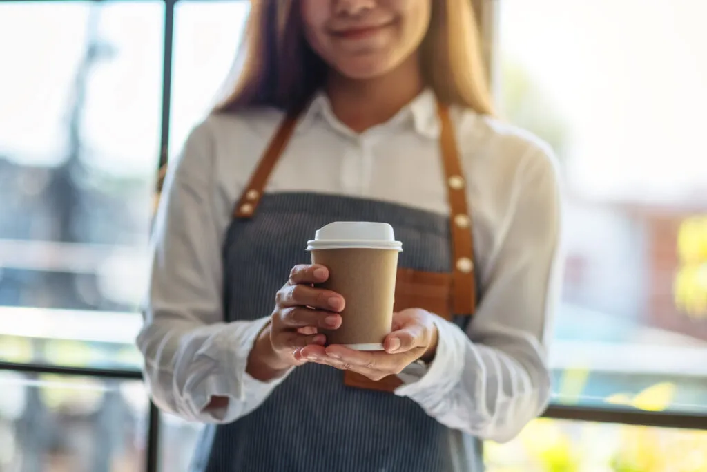 Young woman holding out paper coffee cup