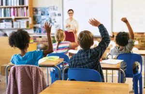 group of students in a classroom with raised hands