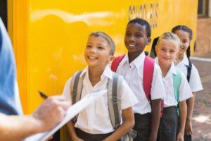 Teacher updating check list of students lined up outside school bus