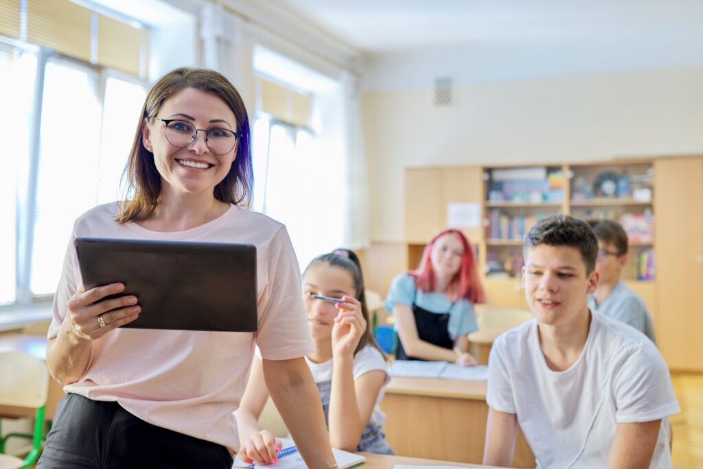 Portrait of female teacher smiling at camera in classroom with teenage students at desks