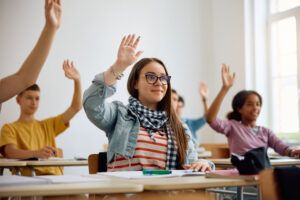 High school student and her classmates raising their hands in class