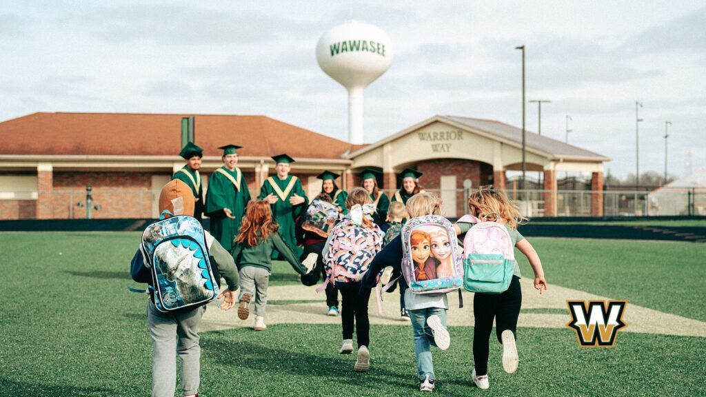 students running on school field in front of Wawasee logo