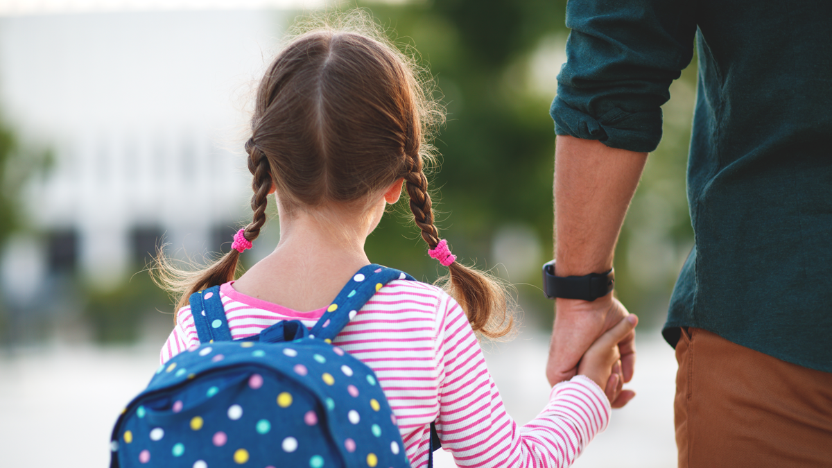 father holds hand of young girl on walk to school