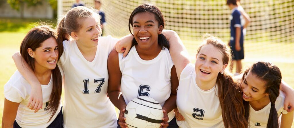 girls soccer team poses smiling on field