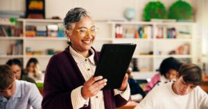 Smiling teacher with tablet taking attendance in classroom