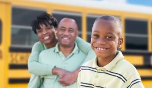 smiling parents and child standing in front of school bus