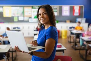Portrait of female teacher holding laptop in classroom