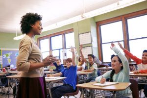 School, teacher and children raise their hands to ask or answer an academic question for learning. Diversity, education and primary school kids speaking to their woman educator in the classroom