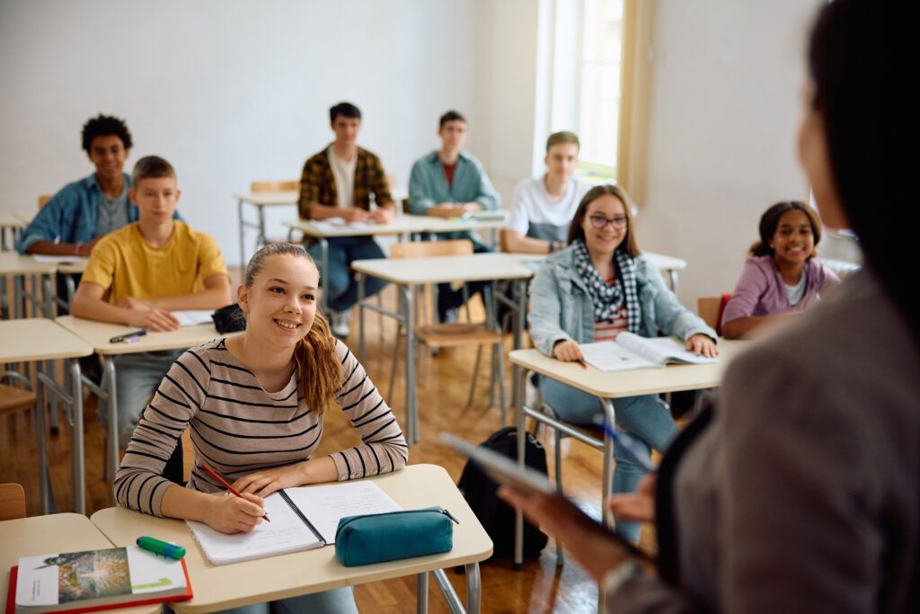 happy classroom of engaged high school students listening to teacher