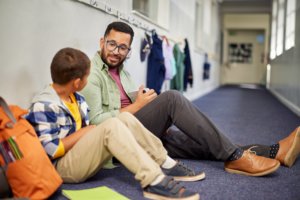 teacher talking to elementary student in hallway outside classroom