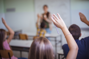 female middle school student in classroom with hand raised