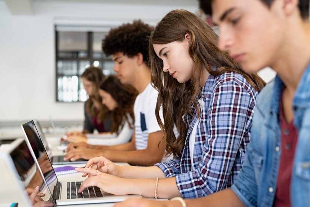 high school students in classroom working on laptops