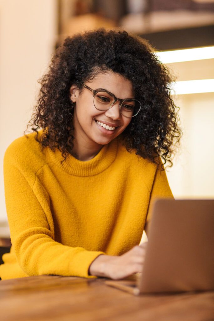 Image of cheerful african american woman in eyeglasses using laptop