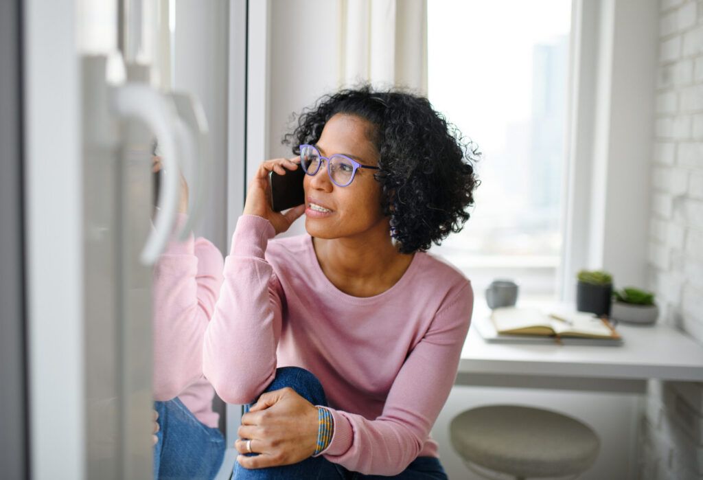 Portrait of happy mature woman making a phone call indoors, looking out of window.