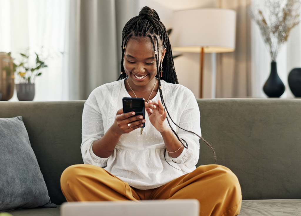 smiling woman reading from phone while sitting on couch at home
