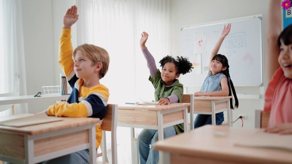 Elementary school students sitting at their desks and raising their hands