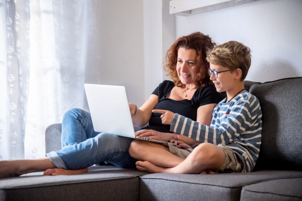 Mother and son sitting on a couch looking at a laptop computer together