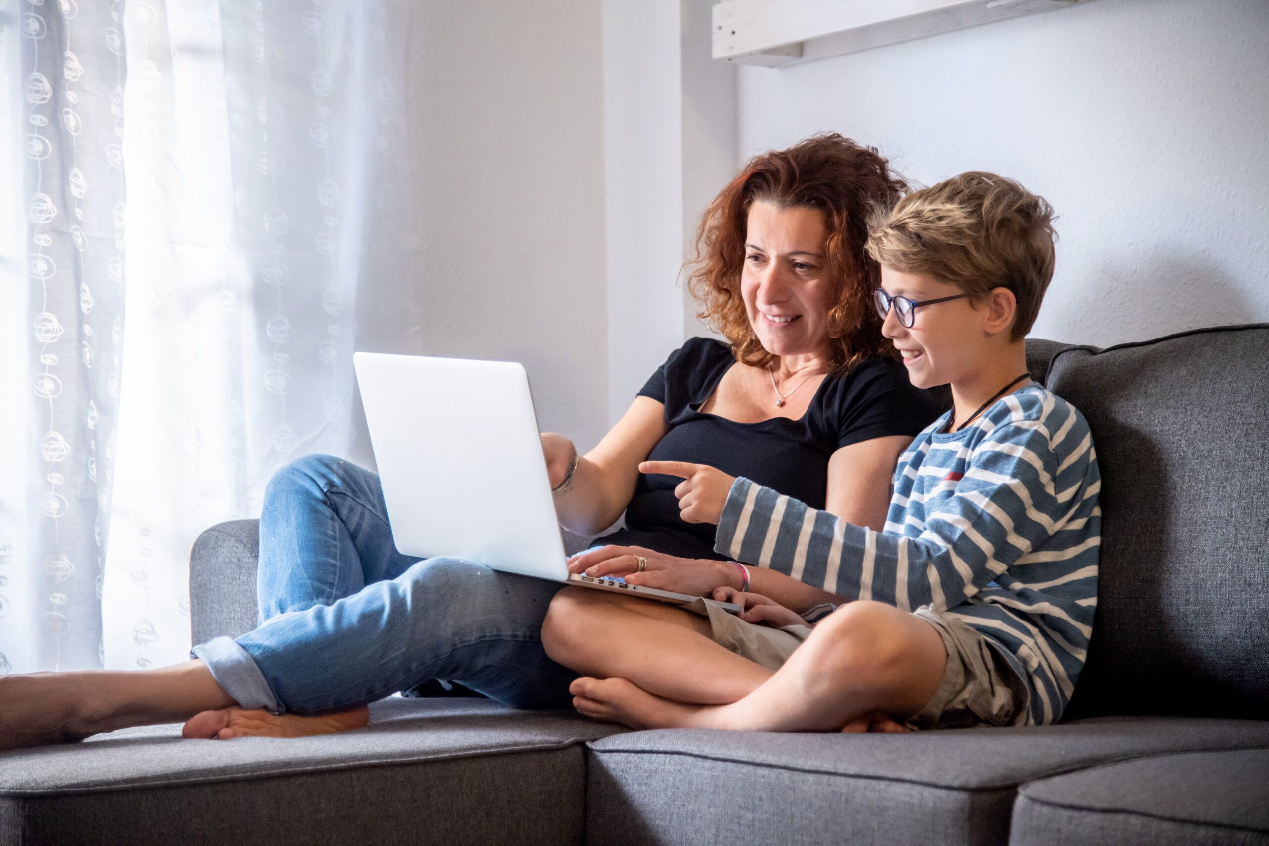 Mother and son sitting on a couch looking at a laptop computer together