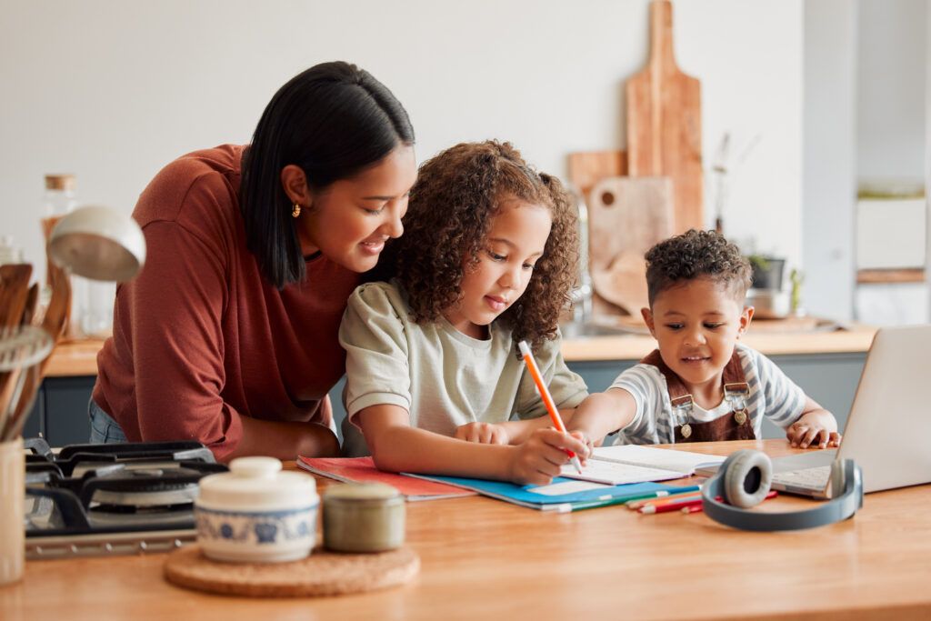 mother supervising young daughter doing schoolwork at kitchen counter