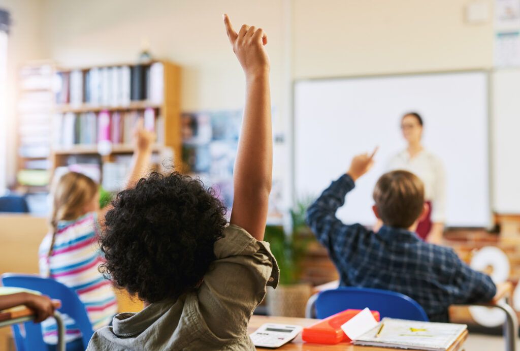 school children in classroom with hands up