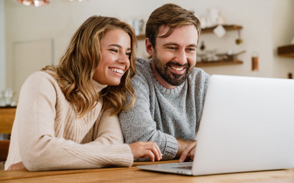 Happy young couple browsing on laptop in their kitchen