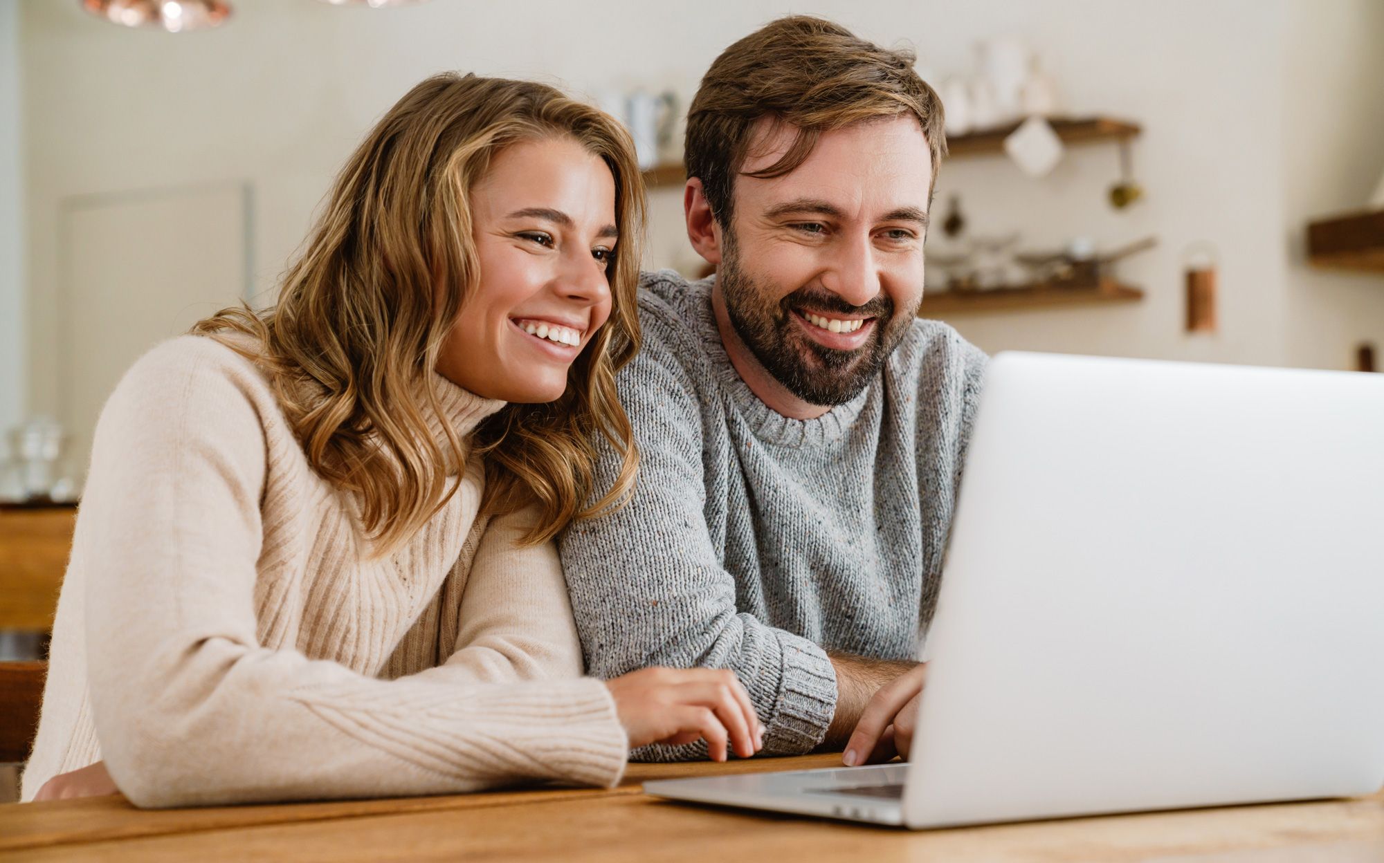 Happy young couple browsing on laptop in their kitchen